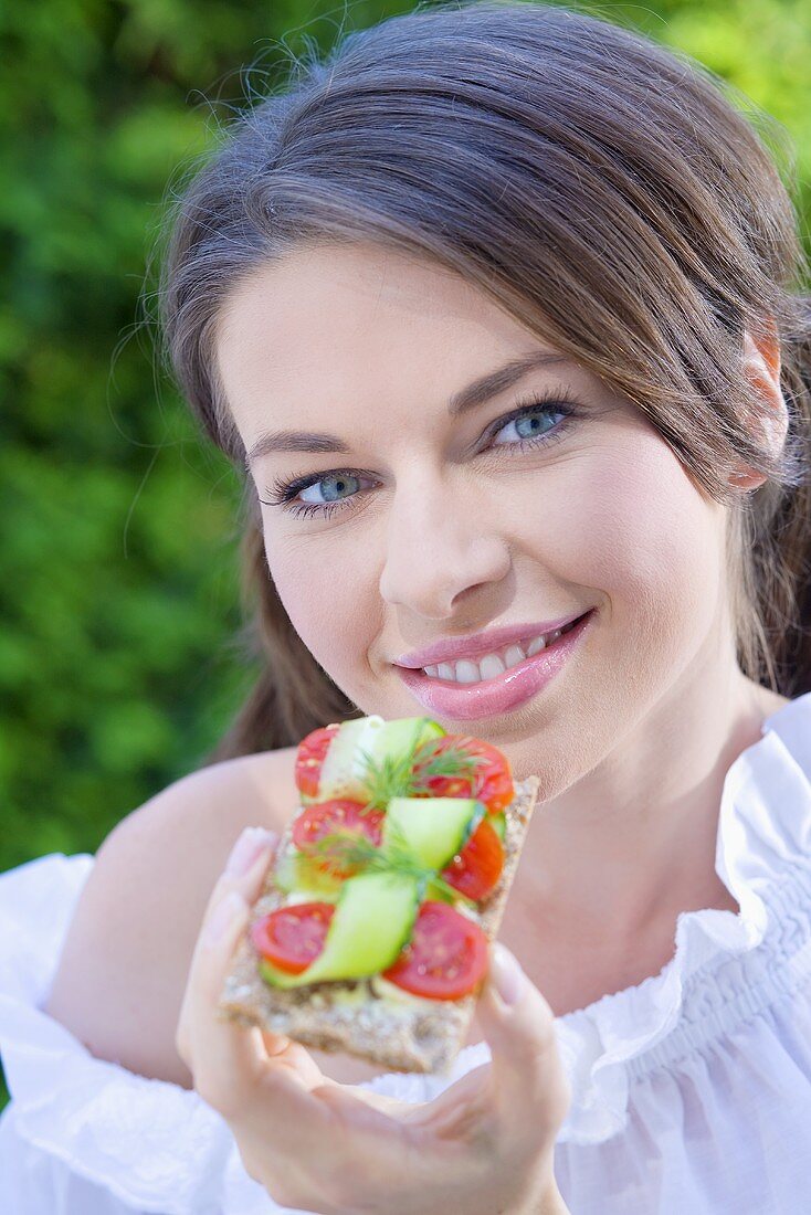 Junge Frau isst Knäckebrot mit Tomaten und Gurken