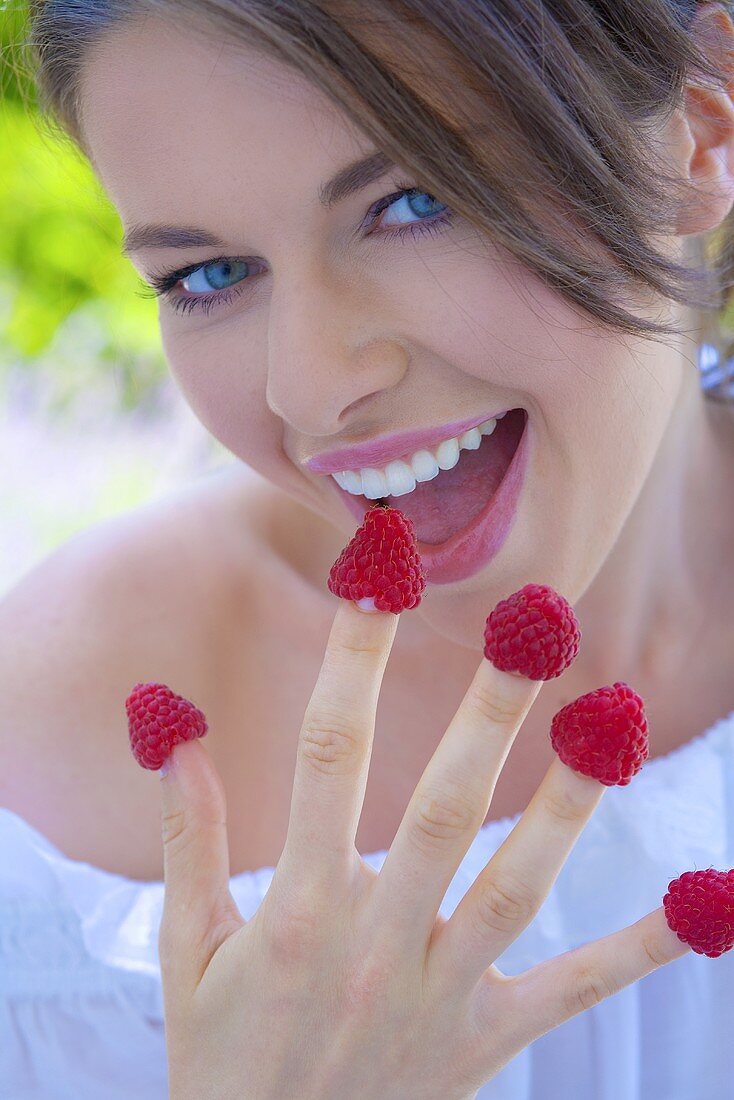 Junge Frau mit Himbeeren auf den Fingern