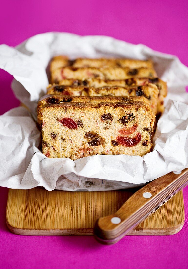 Several slices of fruit loaf in paper on chopping board