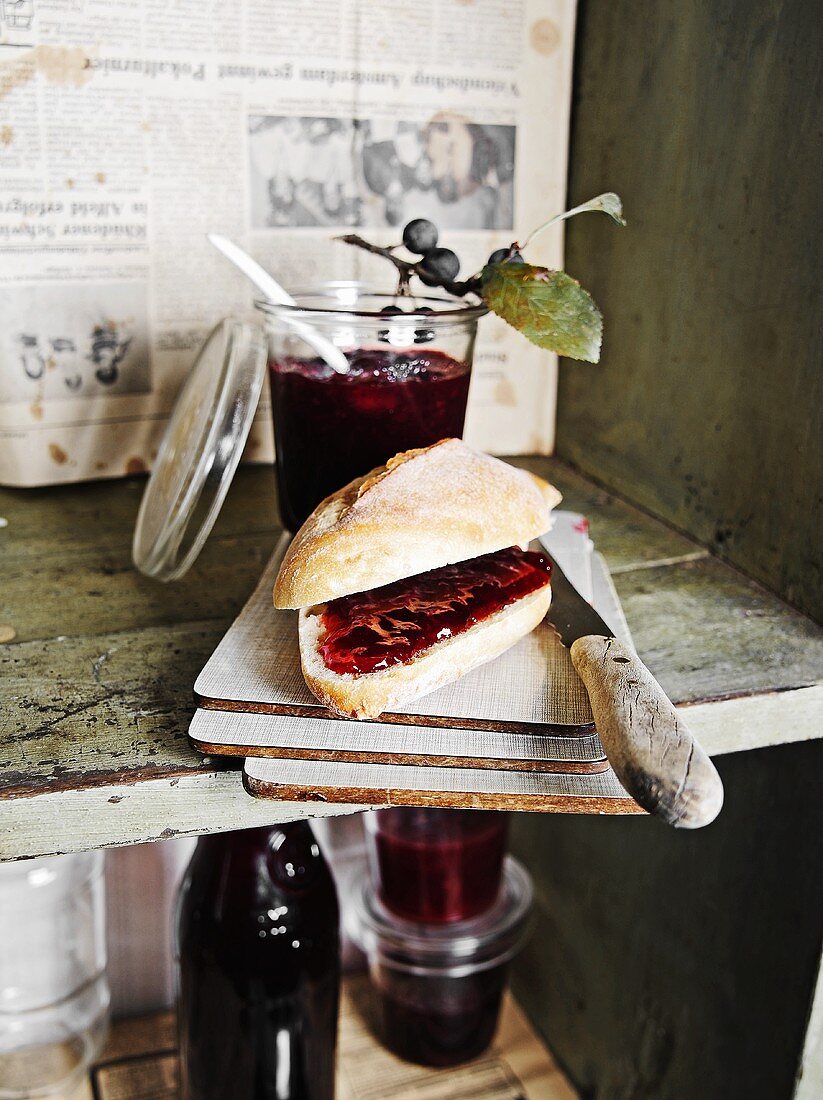 Bread roll filled with cherry jam and several jars of jam on shelf