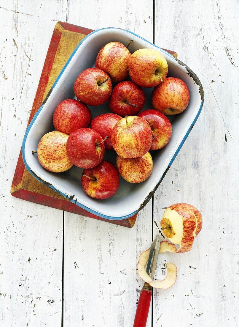 Red apples in enamel dish, half-peeled apple beside it