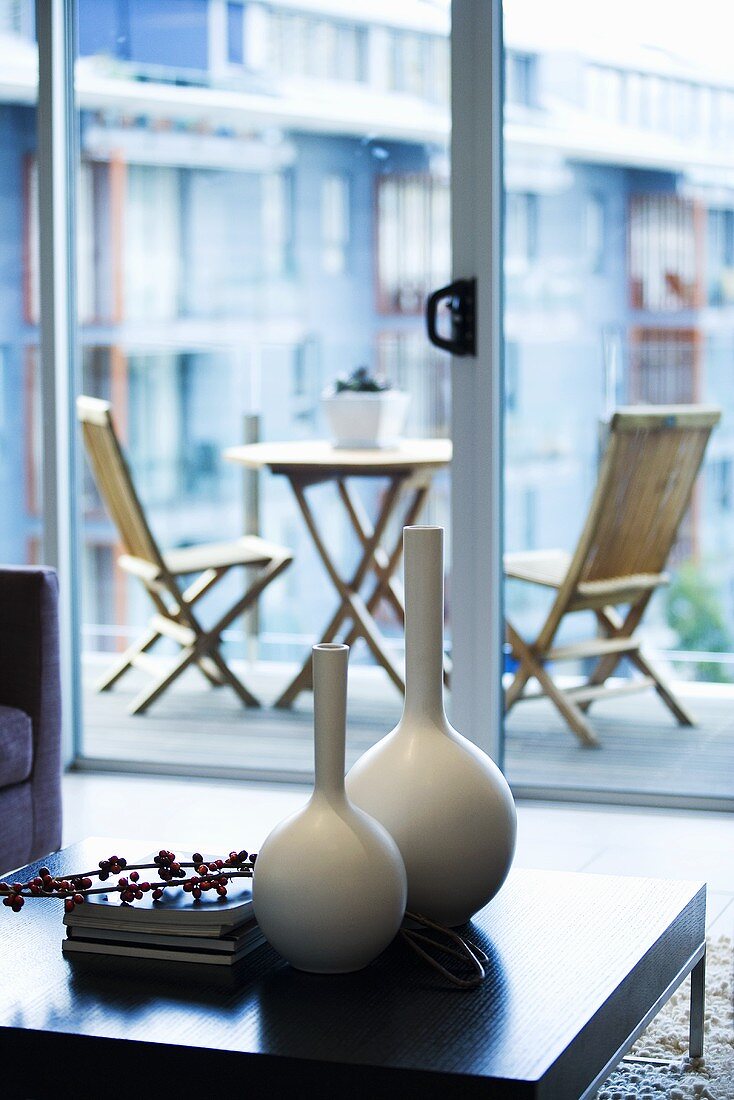 Deko-Vasen & Bücher auf Couchtisch eines Wohnzimmers, im Hintergrund Balkon mit Tisch & Stühlen