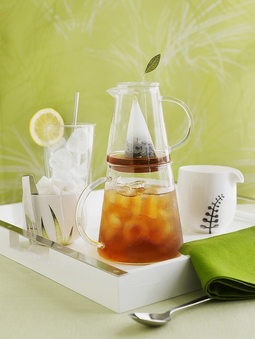 Iced tea in jug, ice cubes and ice tongs