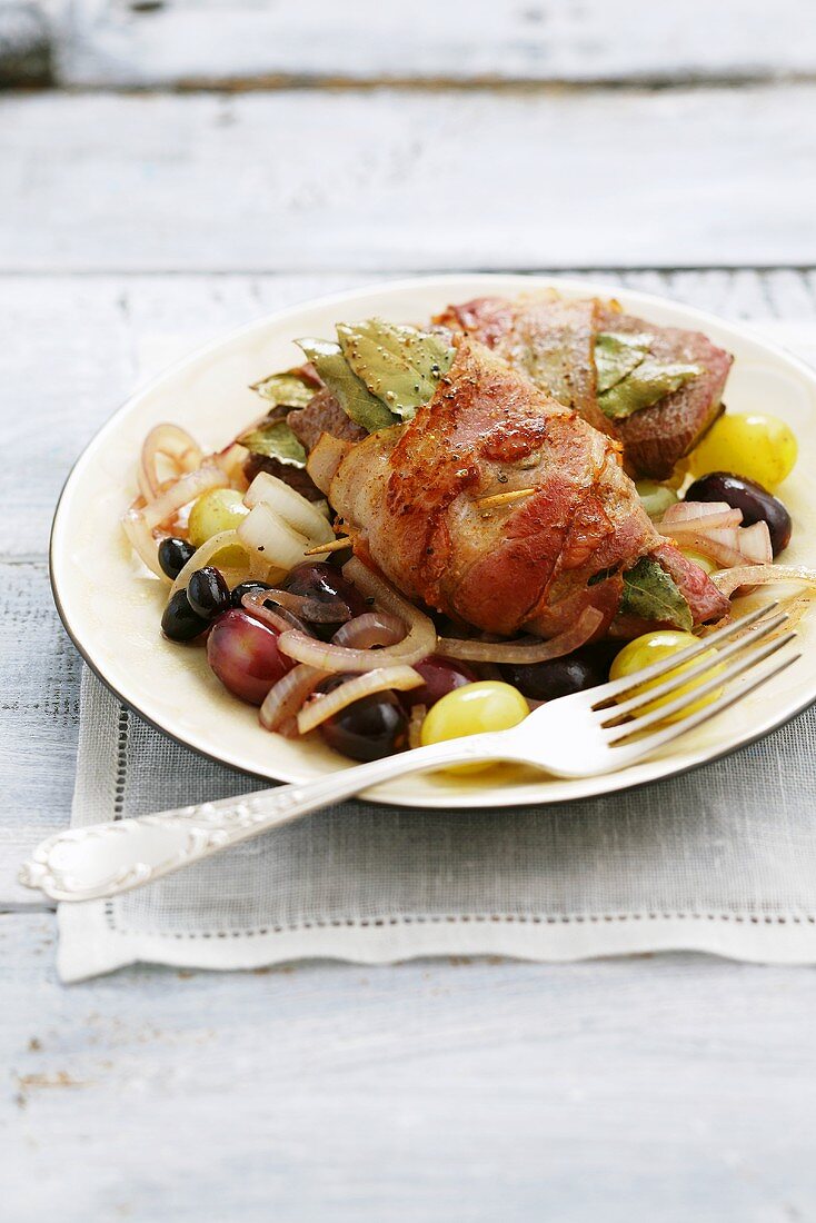 Bacon-wrapped sirloin steak with bay leaves on onions and grapes