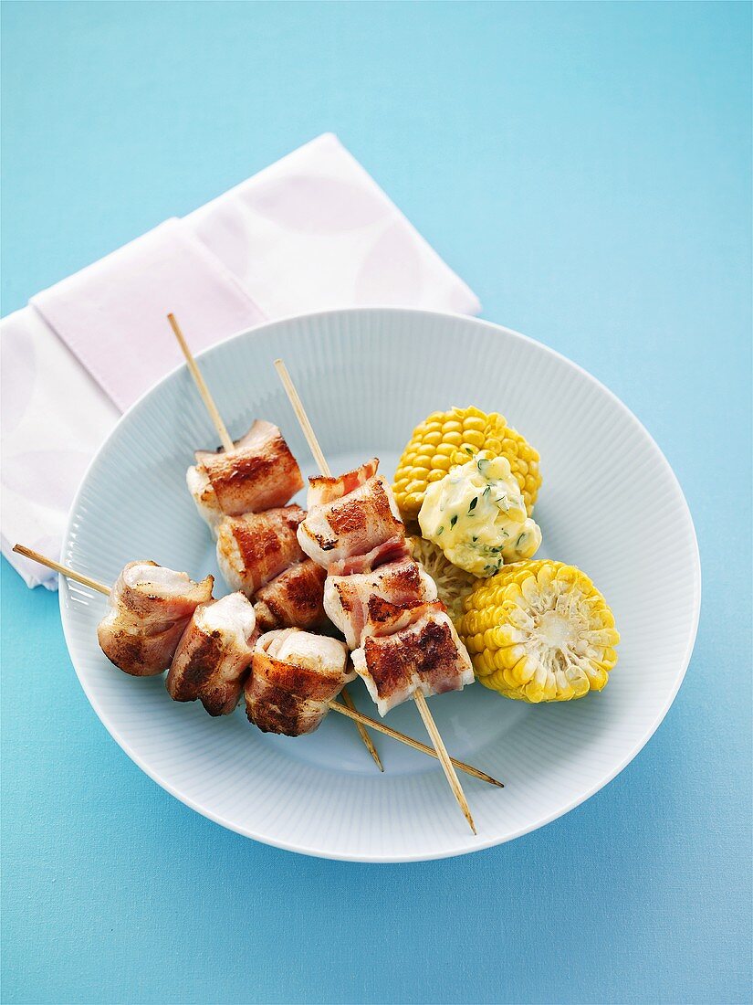 Bacon-wrapped chicken skewers with corn on the cob and herb butter