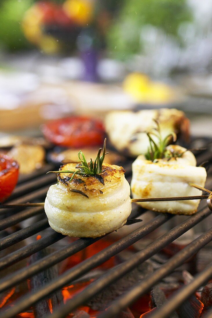 Eel rolls with rosemary and tomato halves on barbecue