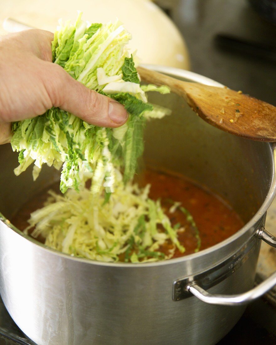 Putting shredded savoy cabbage into a soup pot