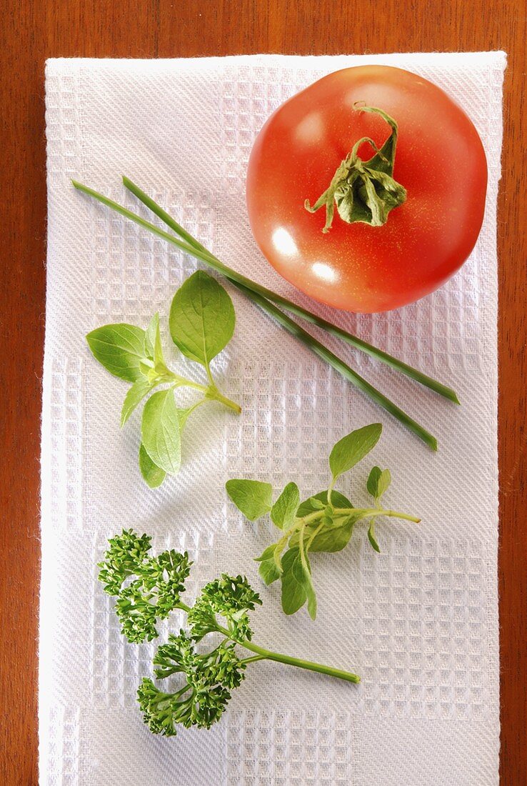A tomato and fresh herbs on white napkin