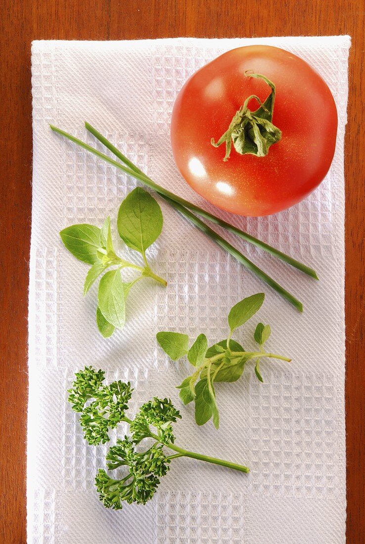 Eine Tomate und frische Kräuter auf weisser Serviette