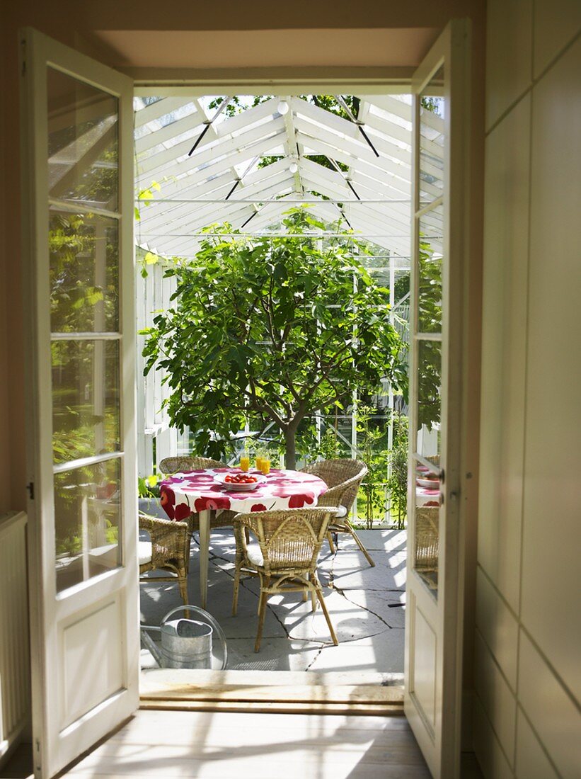 Blick in einen Wintergarten: Tisch mit Korbstühlen