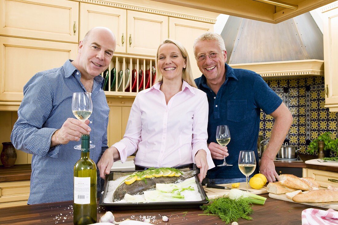 Friends with fish and white wine in kitchen