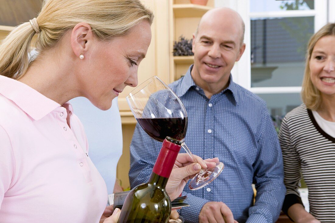 Woman smelling bouquet of red wine, couple watching with interest