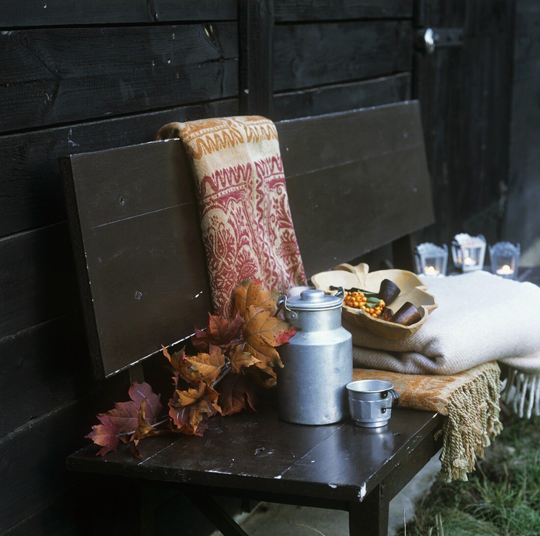 Autumn leaves, milk can, cup, sea buckthorn & throws on bench