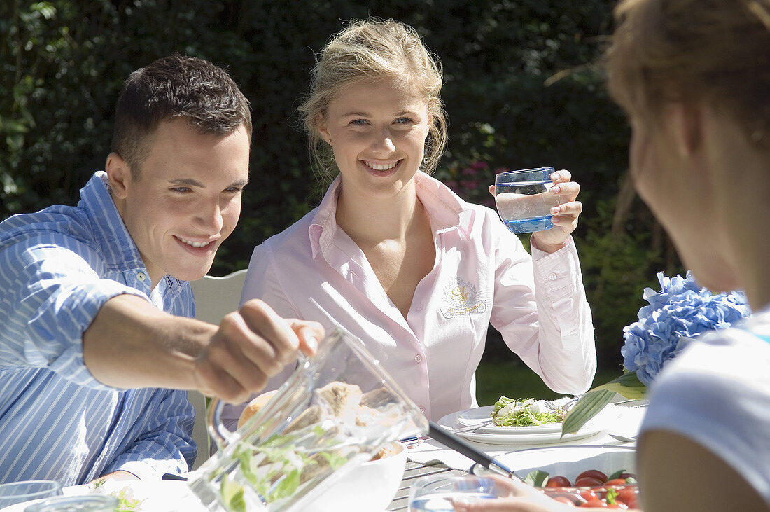 Junge Leute mit Vorspeisen und Wasser am Tisch im Freien