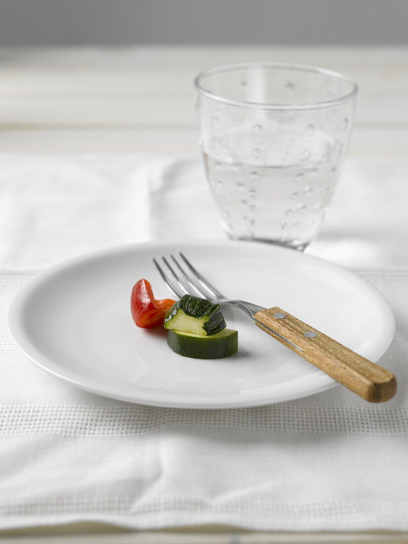 Zucchini und Paprika auf weißem Teller und ein Glas Wasser