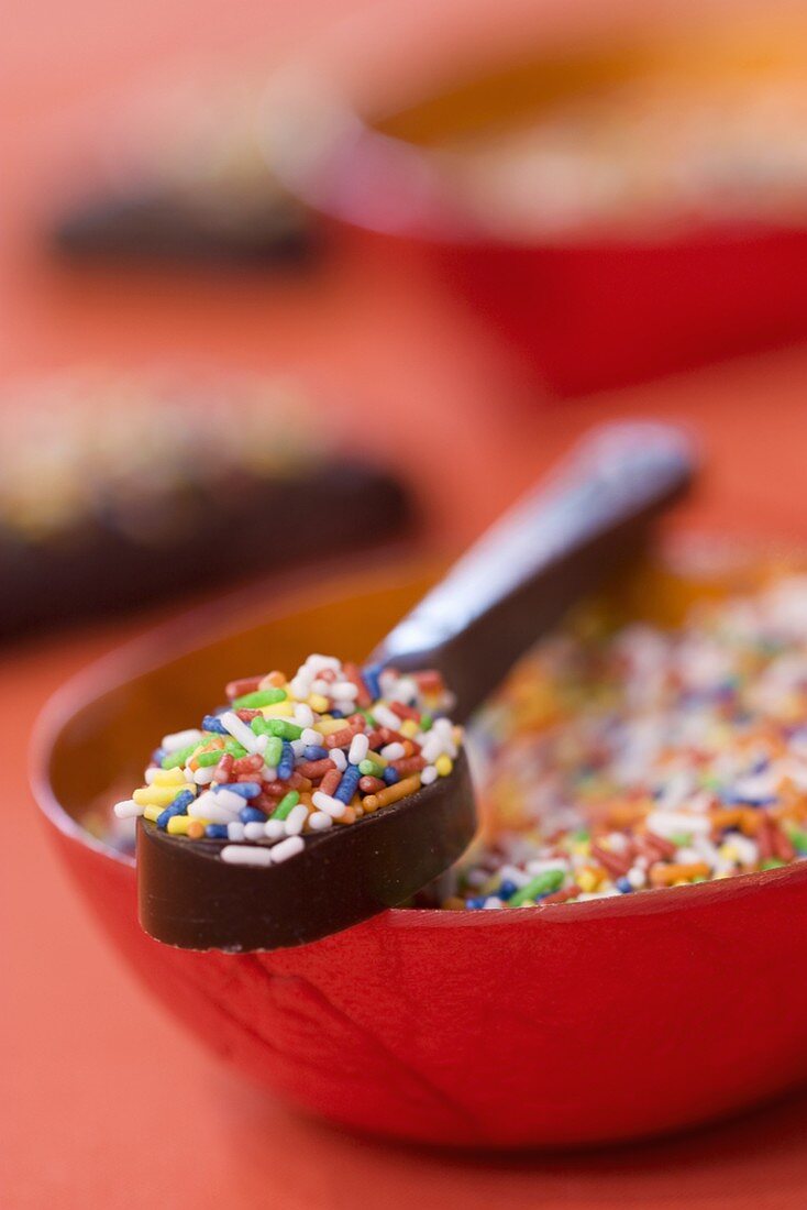 Sprinkles in a small bowl and on a chocolate spoon