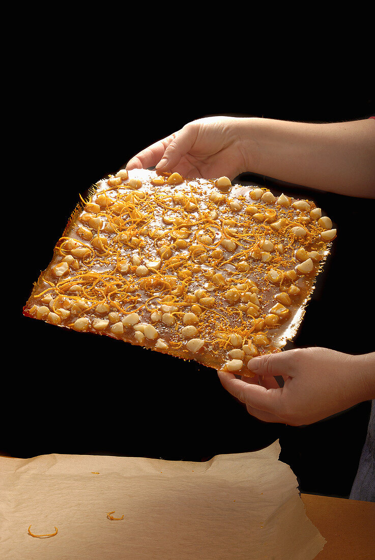 Hands holding macadamia nut brittle with orange peel & pepper