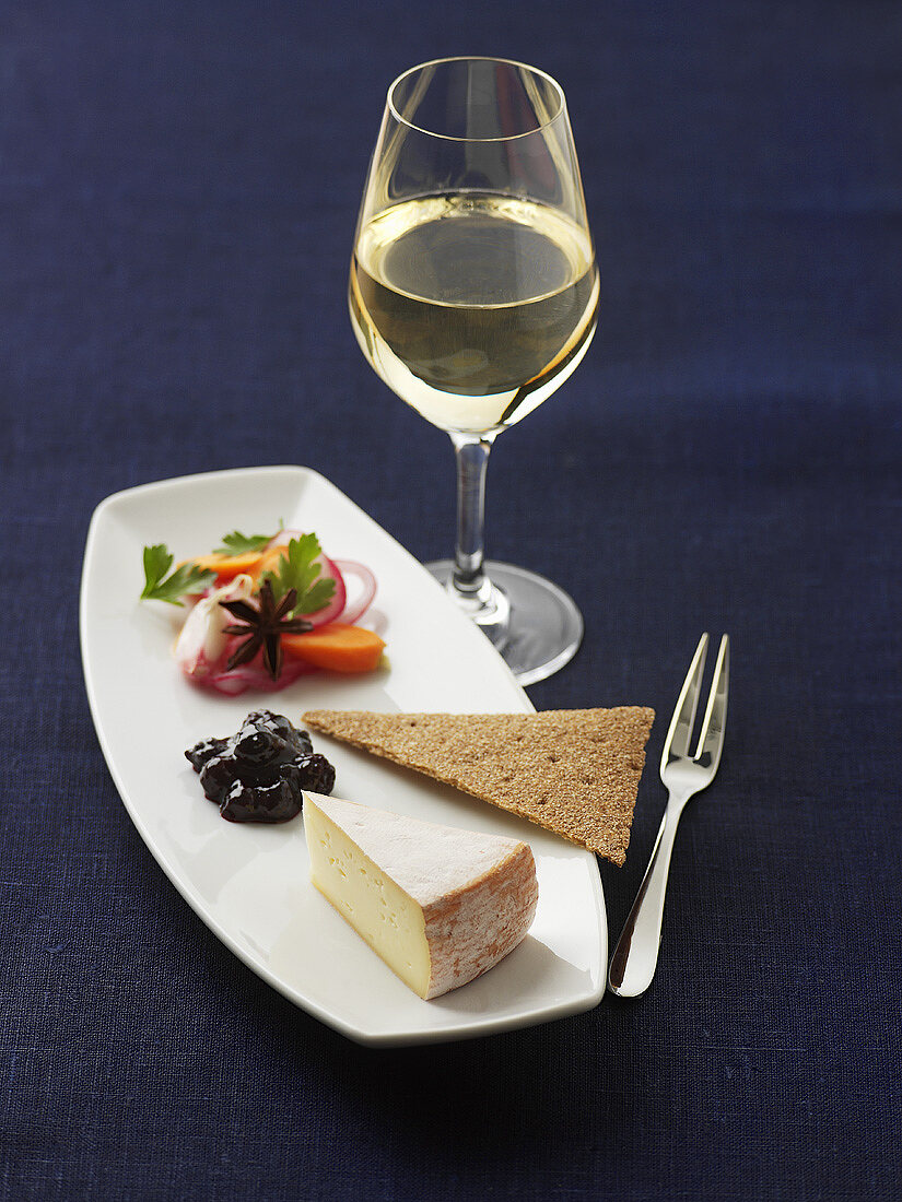 A piece of cheese with crispbread and white wine