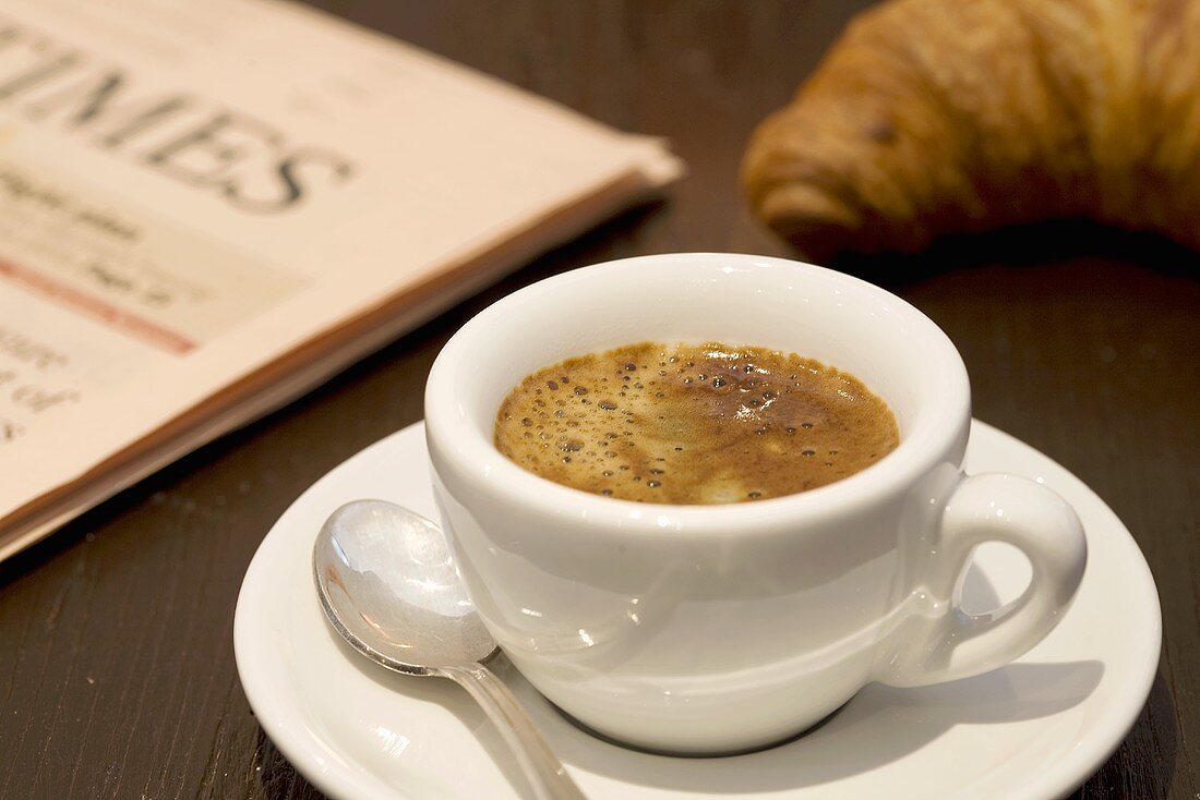 A cup of espresso, a newspaper and a croissant