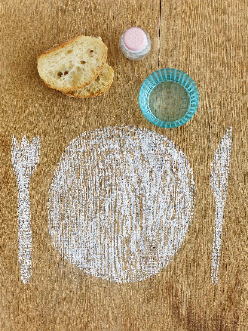 Mit Kreide gemaltes Gedeck, Wasser, Brot und Salz auf Holzuntergrund