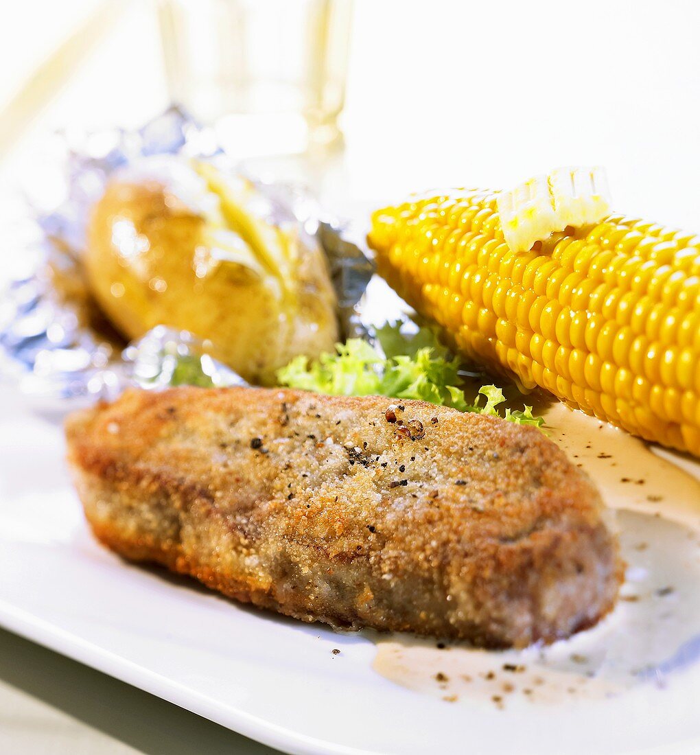 Breaded beef steak with corn on the cob and baked potato