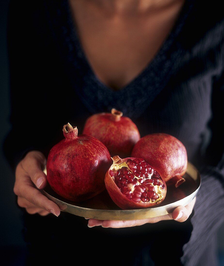 Hands holding tray of pomegranates