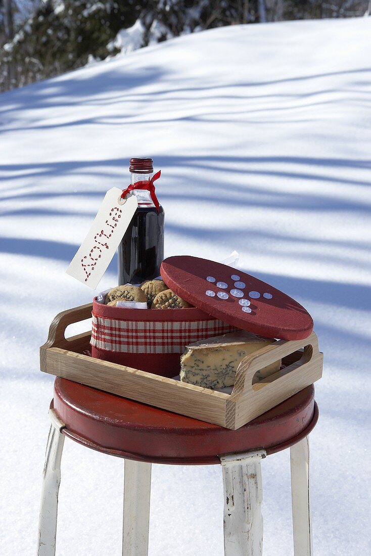 Tablett mit Rotwein, Plätzchen und Käse auf Stuhl im Schnee