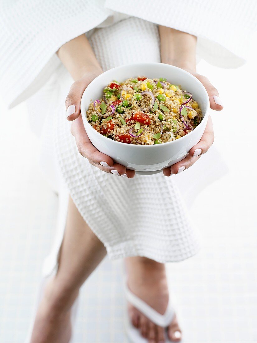 Person in bathrobe holding small bowl of quinoa salad
