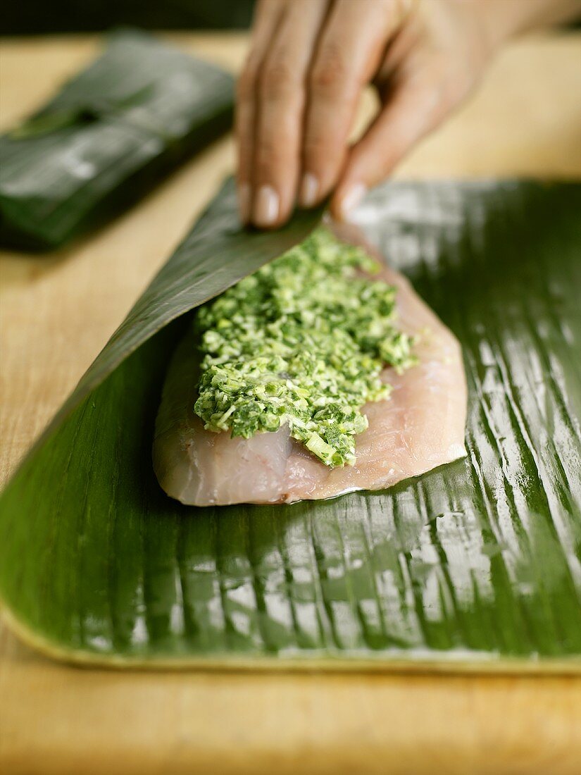 Wrapping fillet of striped bass with herb paste in banana leaf