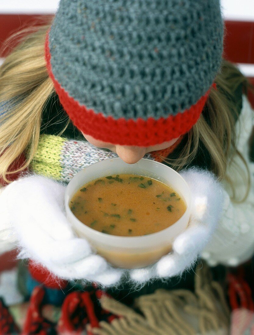 Mädchen in Winterkleidung trinkt heiße Suppe