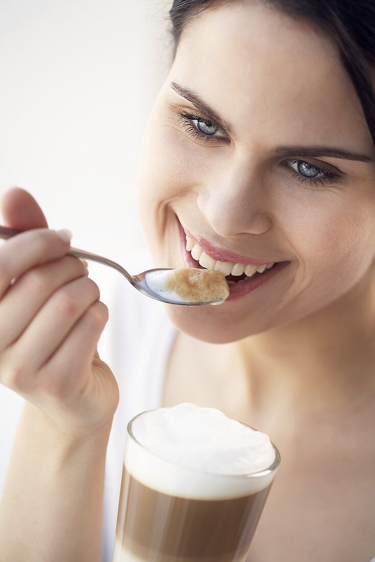 Young woman eating milk froth from latte macchiato with spoon