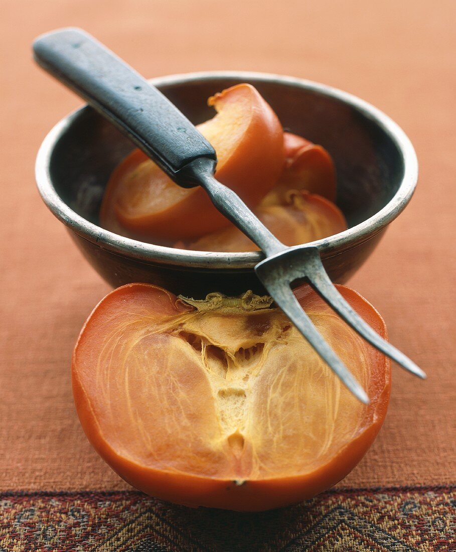 Persimmon in and beside metal bowl with carving fork