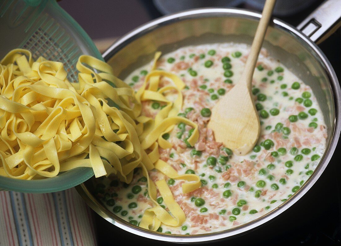 Mixing ribbon pasta with ham and cream sauce