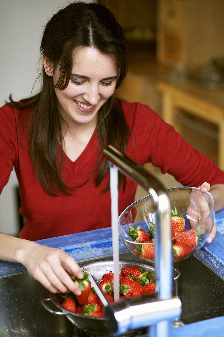 Junge Frau wäscht frische Erdbeeren