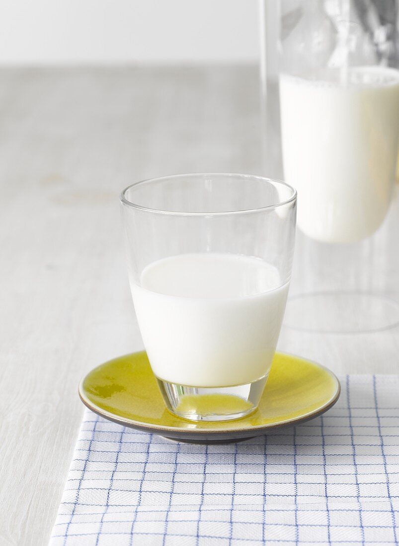 A glass of milk, glass carafe of milk in background