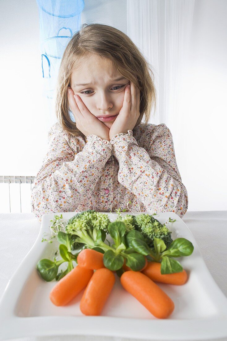 Girl sitting sadly in front of a plate of vegetables
