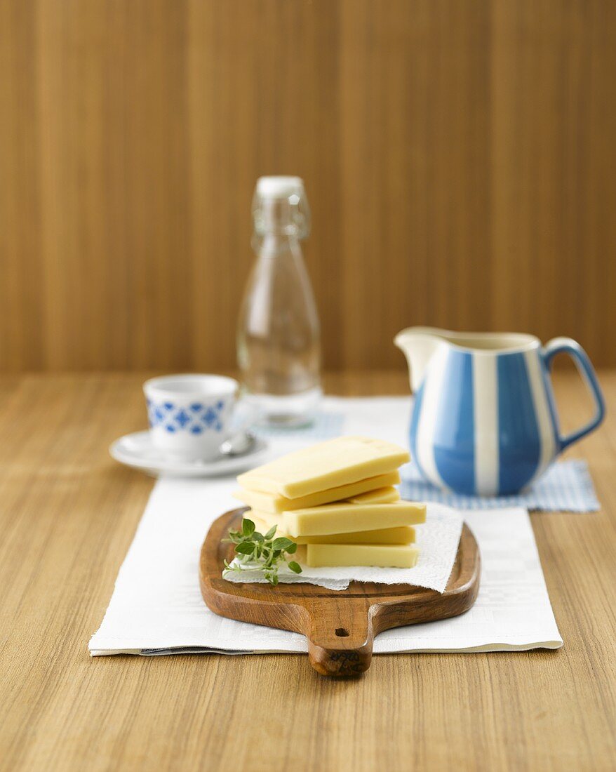 Thick slices of cheese on wooden board, milk jug, cup, bottle