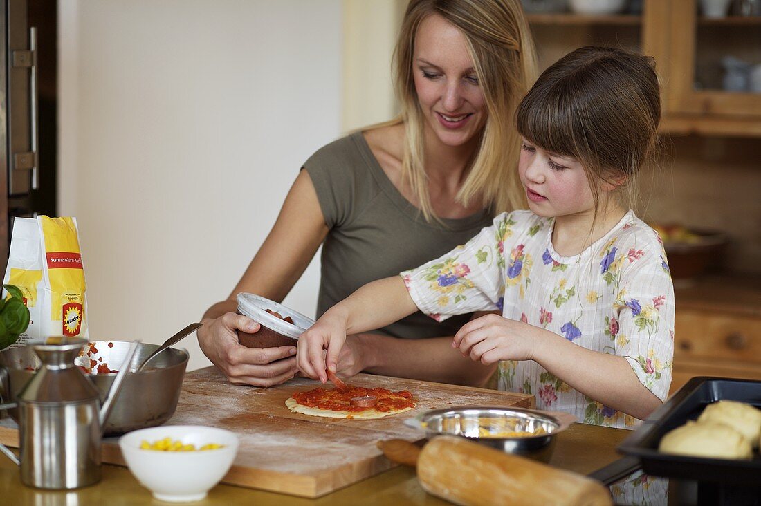 Mother and daughter putting topping on a mini-pizza