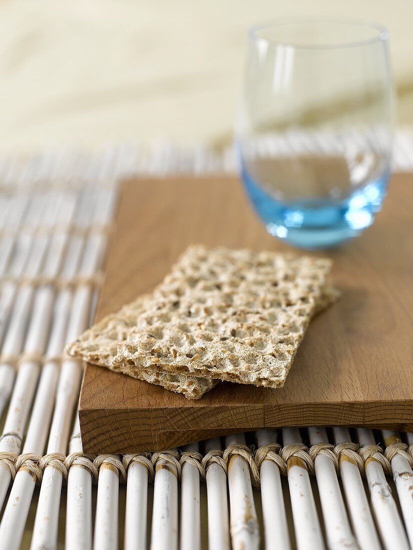 Wholemeal crispbread and tumbler on wooden board