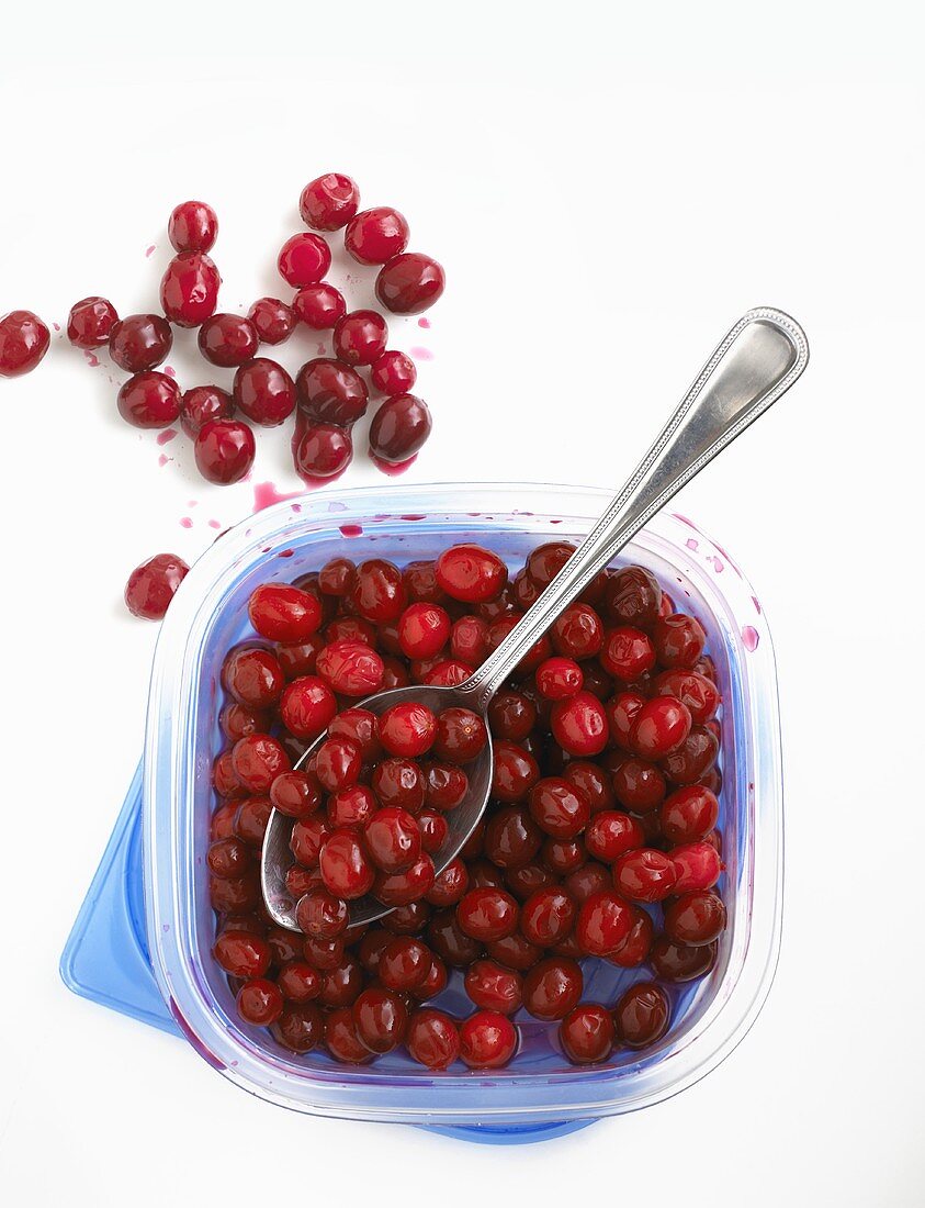 Cooked cranberries with spoon in a plastic box