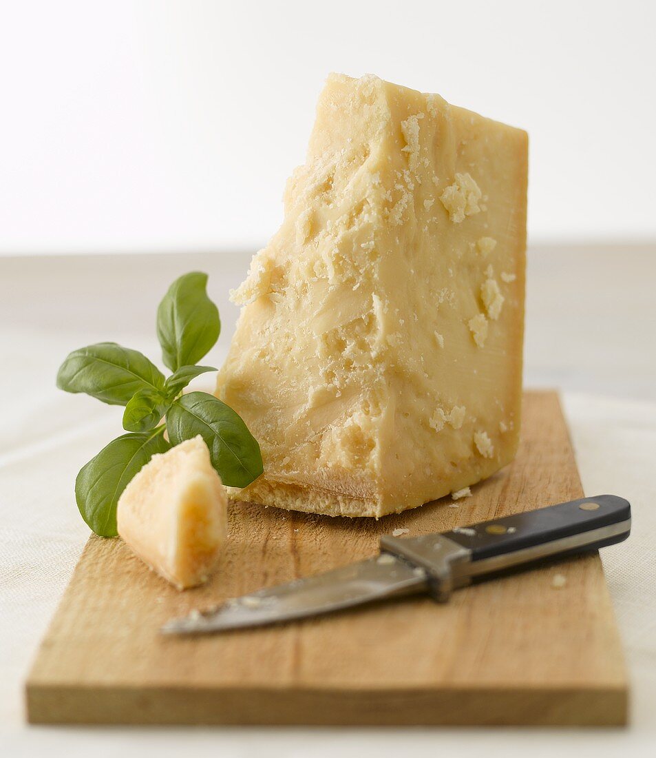 Parmesan with basil and knife on wooden board