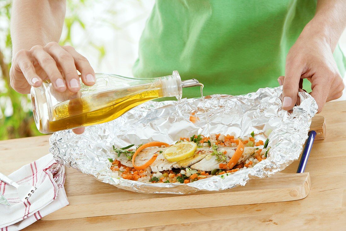 Drizzling fish & vegetables in foil with olive oil