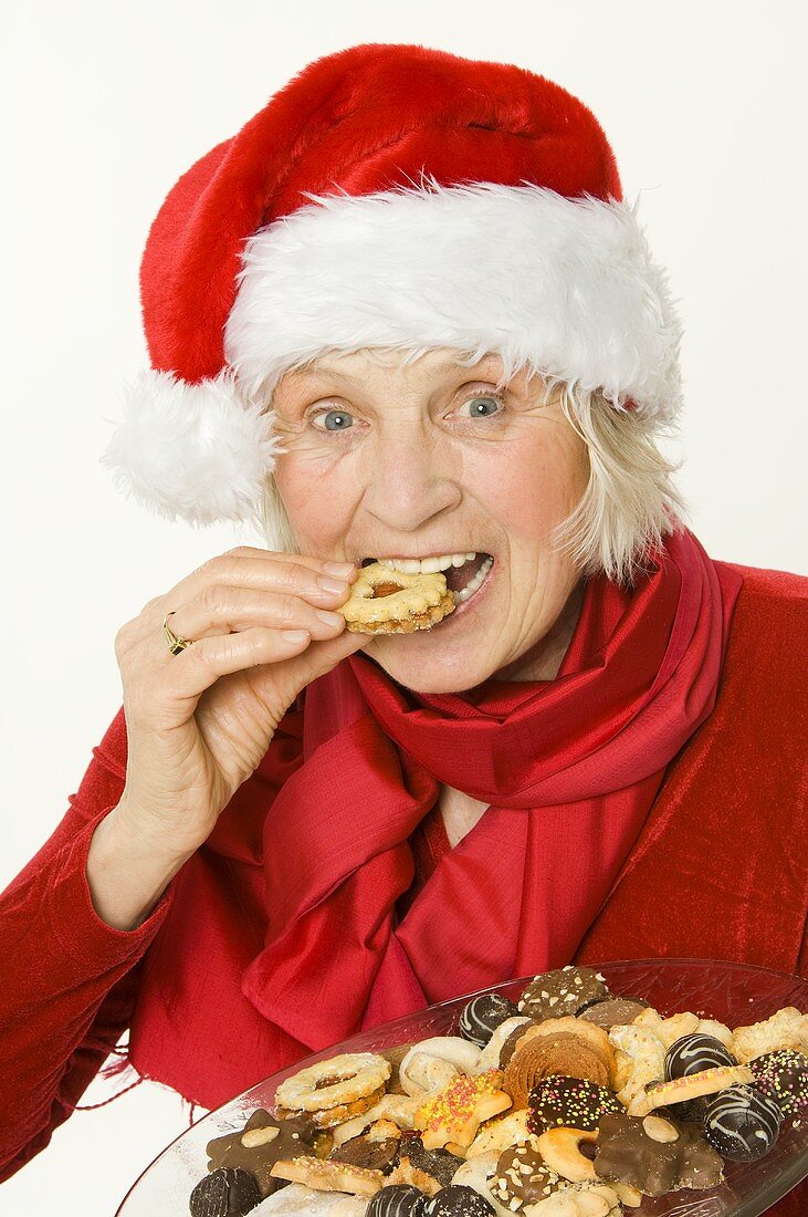 Elderly lady in Father Christmas hat eating a biscuit