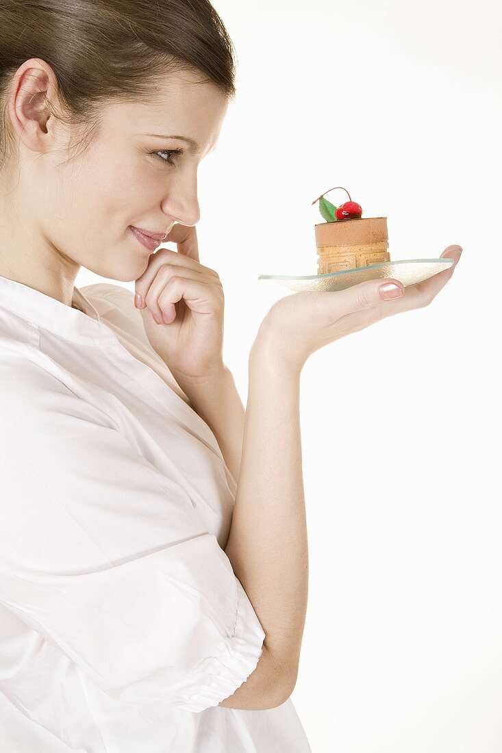 Young woman holding a small cake on a glass plate