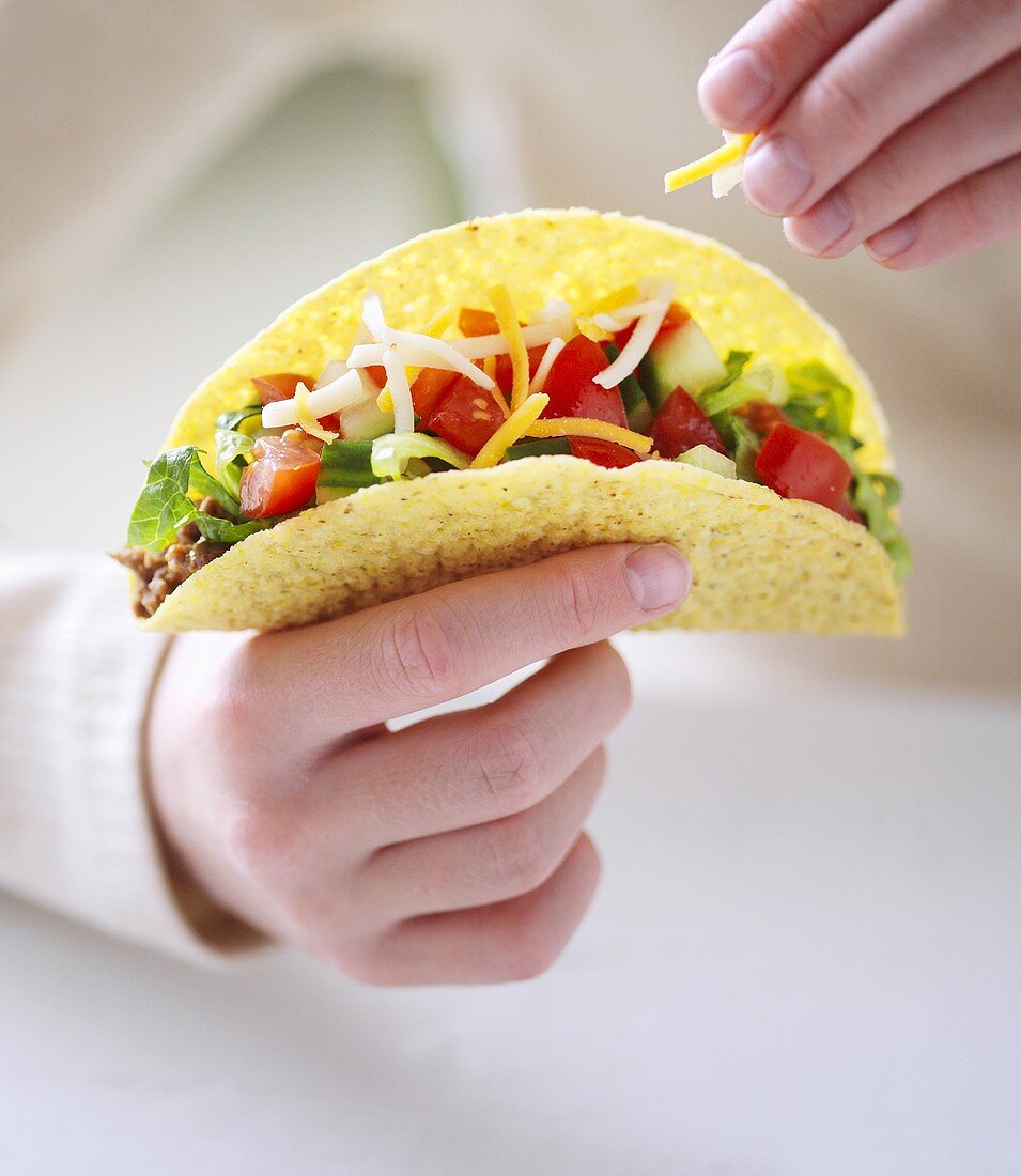 Hand hält Taco mit Salat und Käse