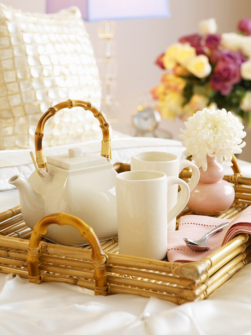 Bamboo tray with tea things and flower on bed