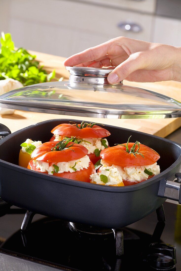 Hand putting glass lid on a pan of stuffed tomatoes