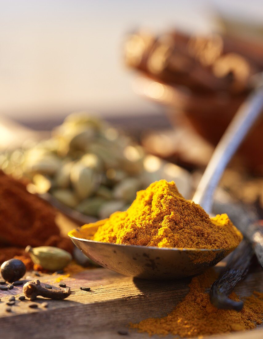 Curry powder on spoon, various spices in background