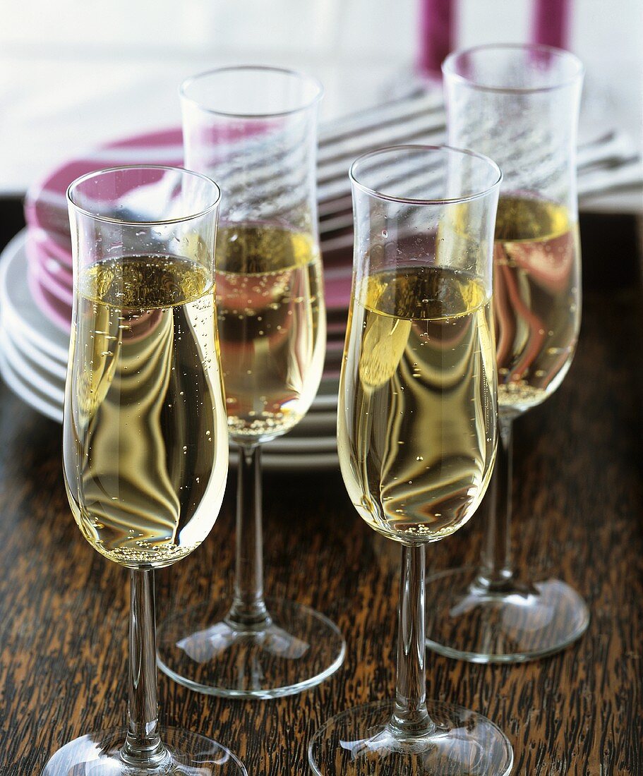 Vier Gläser Champagner, dahinter Tellerstapel und Besteck