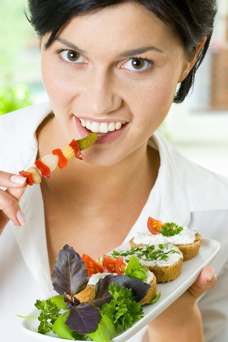Young woman eating pickled vegetables from a cocktail stick
